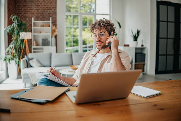 istock Young man engaged in freelance work at home office while on a phone call in a modern living room 2225358385