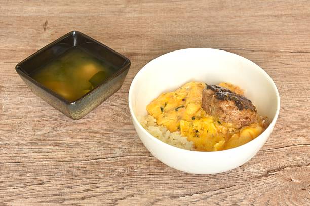 grilled hamburg pork steak and creamy egg omelets topping on rice in white bowl with miso or soy sauce soup