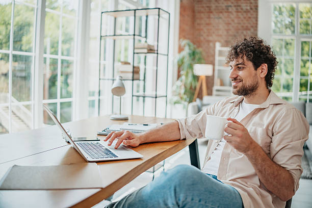 istock Young man works from home enjoying a cup while typing on his laptop in a modern living space 2225359582