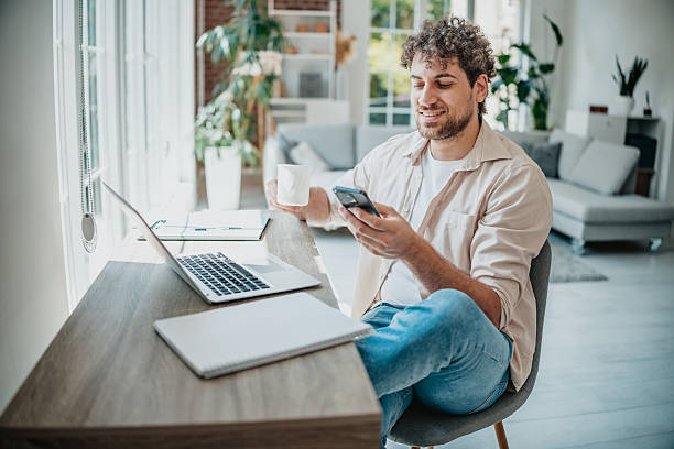 istock Young man works from home, using laptop and phone while enjoying coffee in modern living room 2225360163