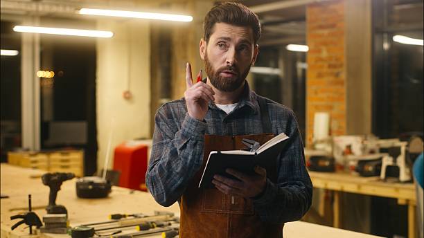 Contemplative Caucasian guy thinking writing notebook in workshop male wood master joiner carpenter lost in thought confused artist man builder planning work project architect idea eureka inspiration