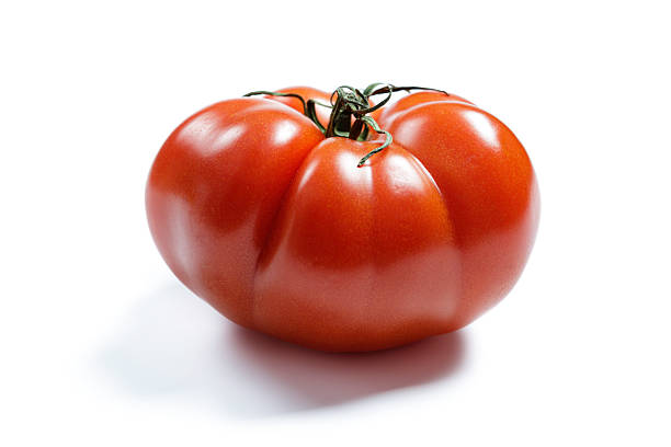 A vibrant red ripe tomato positioned on a clean white background. Showcasing its natural texture and leafy green stem, this image highlights the fresh, organic essence of the fruit, commonly associated with healthy eating, gardening, and culinary ingredients. Perfectly lit, it conveys freshness and vibrancy.