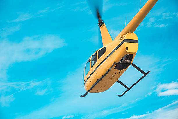 istock Yellow Helicopter in Flight Against Clear Blue Sky, Rear Underside View 2225363232