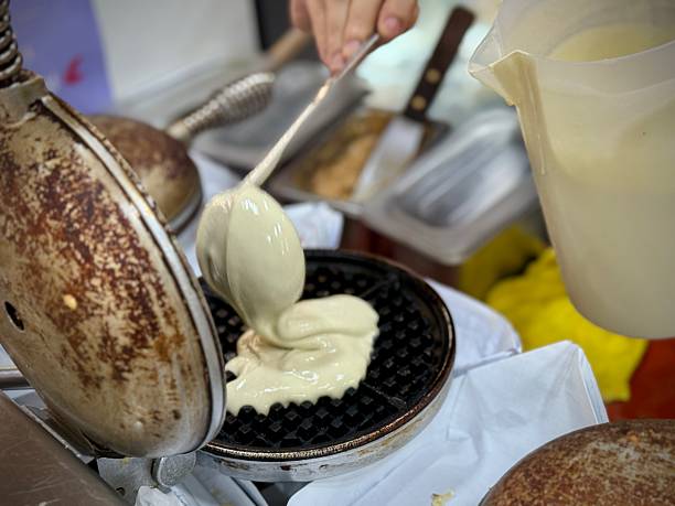 istock Waffle seller scooping waffle pancake raw mix onto toaster 2225363352