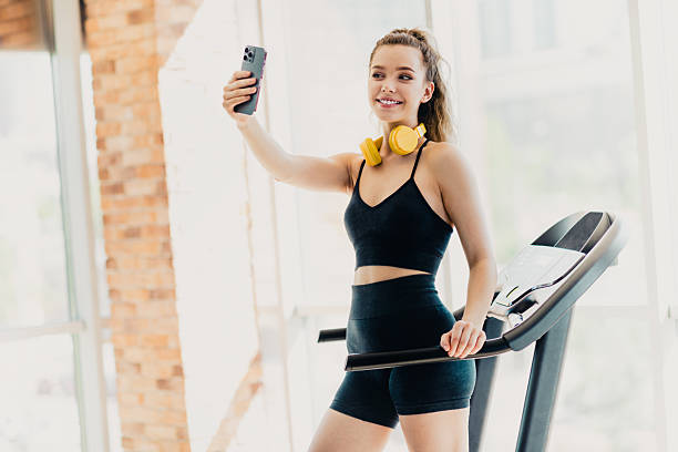 istock Active woman in activewear taking a selfie on a treadmill during her cardio workout in a light-filled gym setting 2225371465
