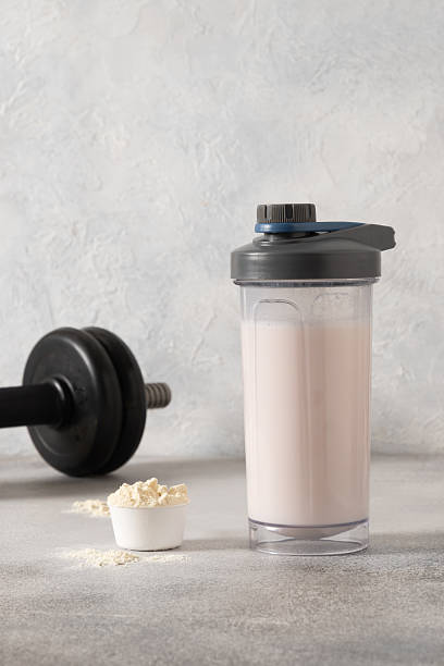 Whey protein shake and dumbbell on gray background.