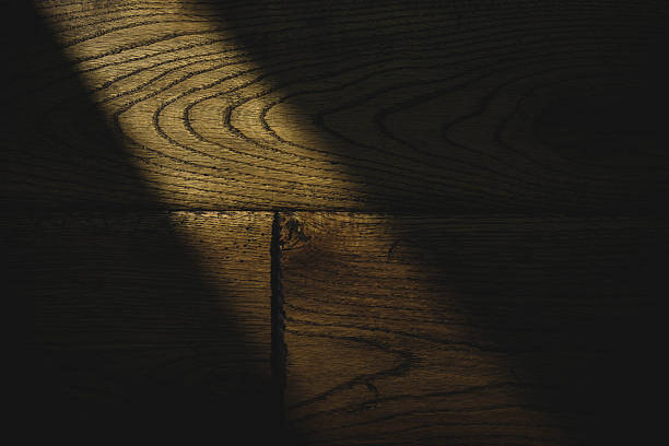 A detailed close-up photograph showcasing the natural wooden texture with its visible and intricate grain patterns. Illuminated by a soft, partially obstructed light source, the image highlights the organic and rustic characteristics of the wooden surface, evoking a sense of nature and craftsmanship.