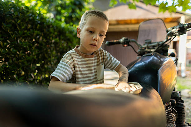 Young boy cleaning a motorcycle with a cloth in a backyard. Early responsibility and hands-on learning concept.