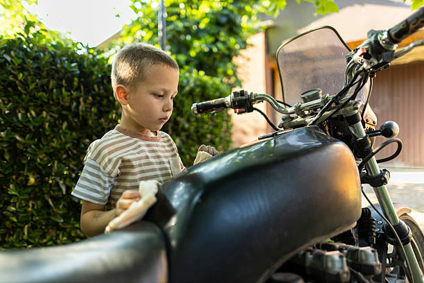 Young boy cleaning a motorcycle with a cloth in a backyard. Early responsibility and hands-on learning concept.