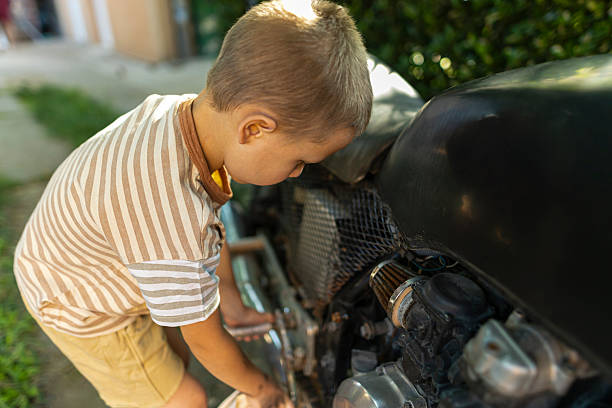 Young boy cleaning a motorcycle with a cloth in a backyard. Early responsibility and hands-on learning concept.