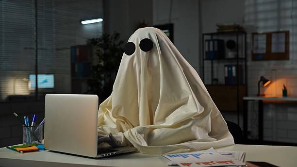 istock Ghost in a Sheet Typing on Laptop in Dimly Lit Office 2225383977