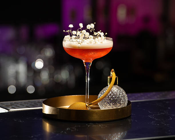 istock blush-toned cocktail with a frothy top is elegantly garnished with delicate white baby's breath flowers, presented on a golden tray alongside a vintage-style perfume atomizer 2225384647
