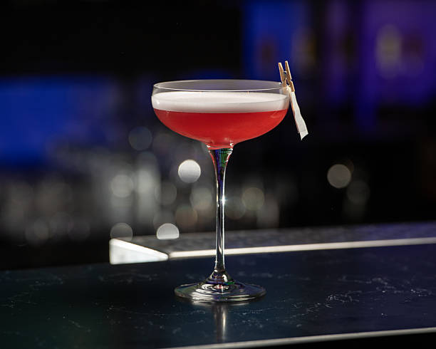 istock A dramatically lit, crimson cocktail with a white foam top is being lit by a bartender, creating a burst of flame from a citrus peel garnish clipped to the glass 2225385710