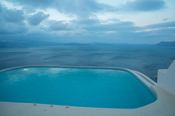 Man sits at the edge of an infinity pool reflecting bright Mediterranean skies