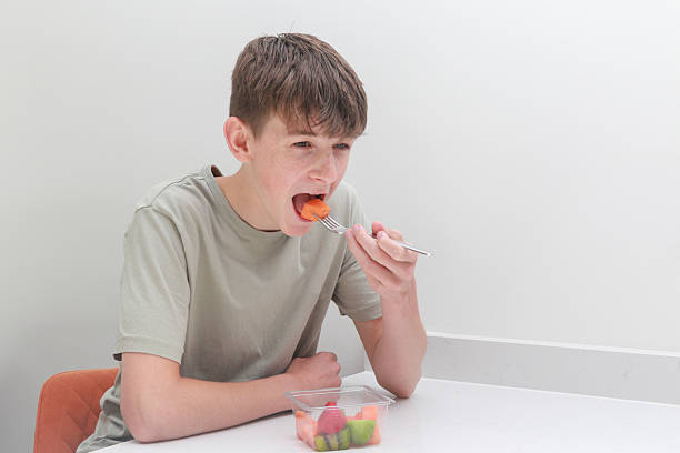 Teenage boy eating freshly prepared, store bought fruit,  with a fork