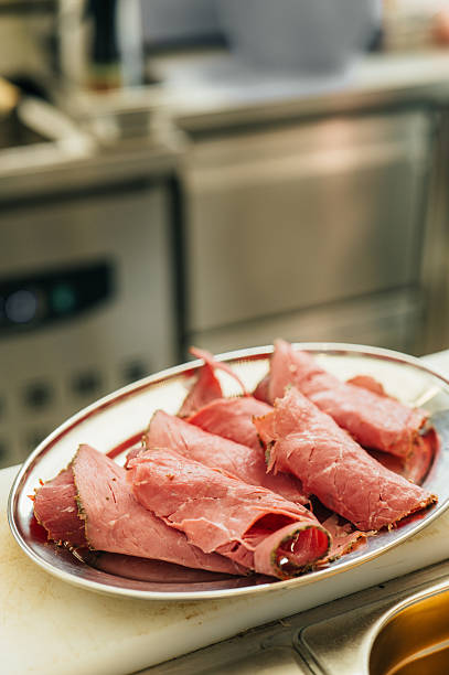 Thin slices of seasoned roast beef on metal platter in restaurant kitchen