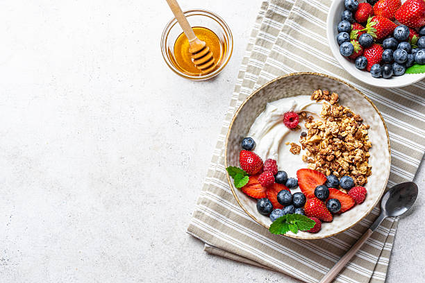 Granola bowl for healthy breakfast. Homemade granola with greek yogurt, fresh berries and honey on white background, top view, copy space. Healthy eating, fitness menu template.