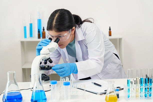 istock Asian high school student wearing safety goggles and lab coat examines biological sample under microscope in classroom, engaging deeply with scientific experiment surrounded by lab tools. 2225411565