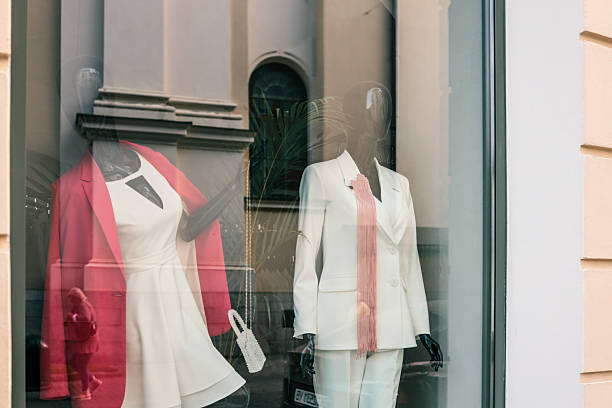 istock Elegant boutique window display featuring two black mannequins dressed in modern women's outfitsâone in a red jacket over a white dress, and the other in a white pantsuit with a pink fringe accessory 2225412139