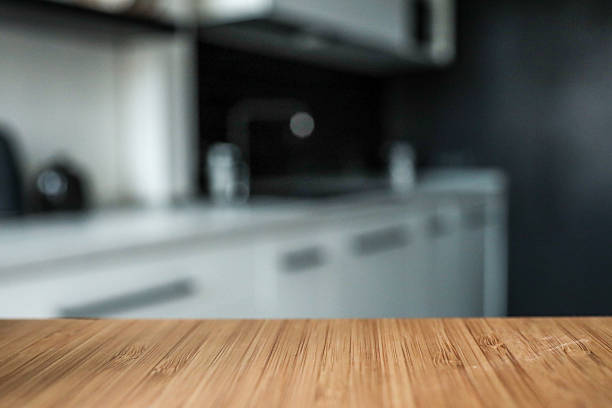 istock Wooden tabletop with blurred modern kitchen in the background. Minimalist design with black and white cabinetry, creating a clean and stylish home interior 2225412156