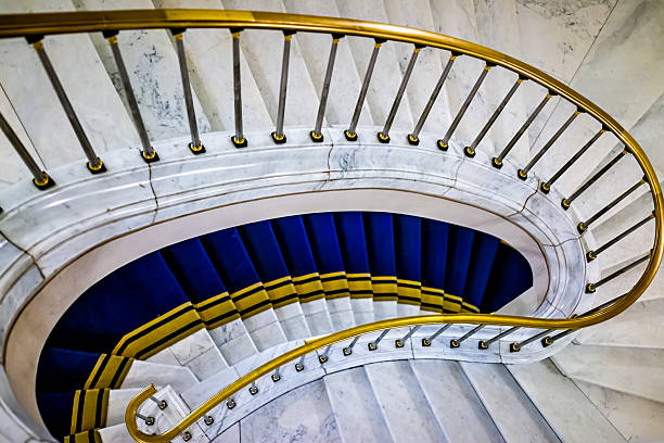 istock Looking down high angle view on spiral marble stone staircase or stairs steps with golden retro vintage railing and blue yellow carpet in Warsaw, Poland 2225414960