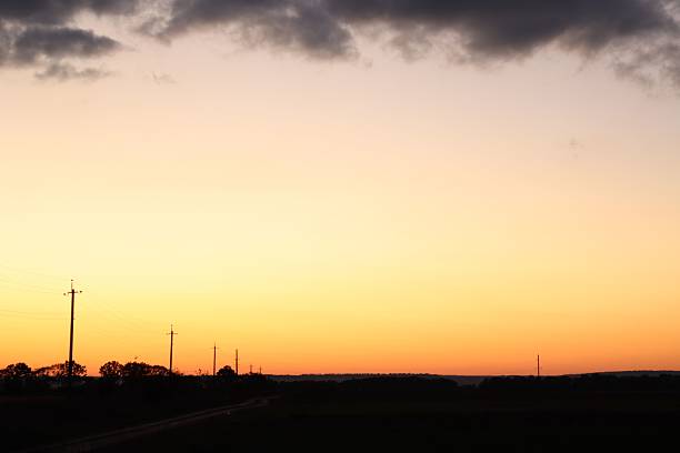 Silhouette of power lines and trees against a vibrant sunset sky with clouds, capturing the tranquil beauty of rural landscapes.