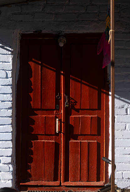 istock Double red wooden doors with strong side light. Red wooden doors in a wall made of bricks covered with blue clay 2225424139