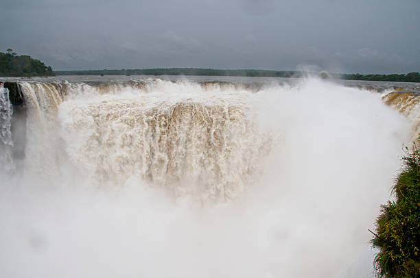 istock Thundering Iguazu Falls generating misty spray through verdant rainforest, dramatic waterfall cascading against overcast sky in Brazilian landscape 2225424175