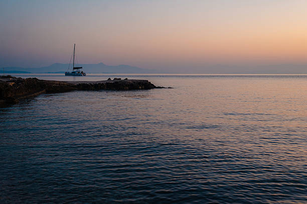 A serene sunset over a calm sea with a sailboat in the distance, creating a peaceful and tranquil atmosphere.