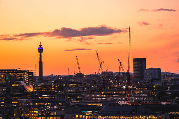 The bt tower stands tall against a vibrant sunset, with construction cranes dotting the london cityscape below