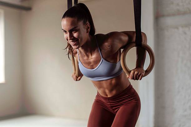 A fit, muscular sportswoman with a determined expression performs a challenging gym ring workout in a fitness studio; She is showcasing strength and athleticism