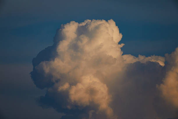 A stunning view of large cumulus cloud formations glowing under the warm, golden hues of sunset. The serene background of the deep blue sky highlights the fluffiness and grandeur of the clouds.