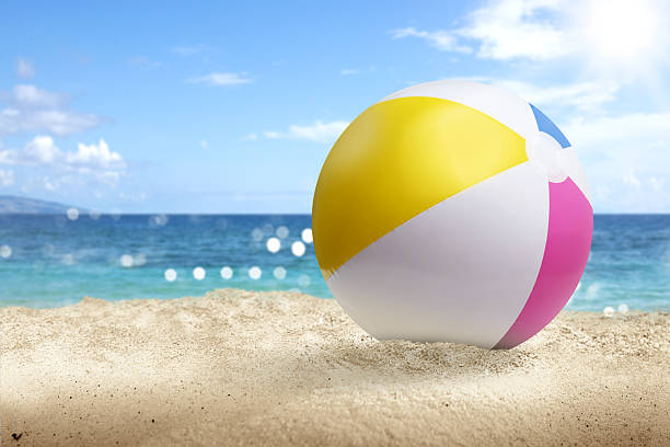 Colorful beach ball on a beautiful sandy beach with an ocean view and a blue sky background. Summer concept