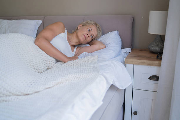 istock Thoughtful woman seated on bed, grasping her stomach softly. 2225471567