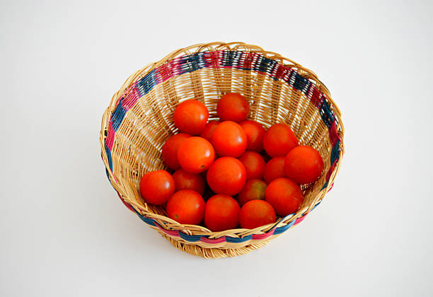A colorful woven basket filled with fresh cherry tomatoes placed on a white surface. The mix of natural textures and vivid red tones creates a vibrant, rustic feel—perfect for themes like farm-to-table, organic produce, or homemade cooking.