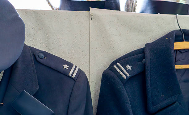 istock Dark blue military uniforms with shoulder epaulettes featuring a single star, hanging on hangers against a light background. 2225495423