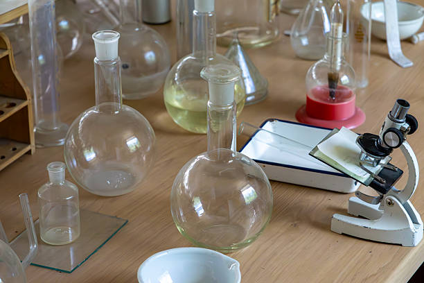 istock Vintage microscope and glass flasks on a laboratory table. Retro chemistry equipment including vessels, enamel tray, and funnel 2225495512