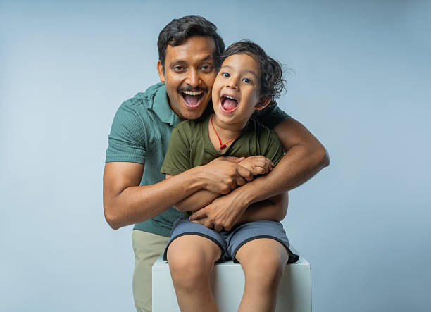 Portrait of happy mid adult father embracing son screaming ecstatically while posing together against white background