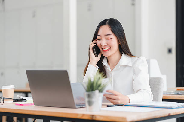 istock Cheerful businesswoman in white shirt is working at her desk, talking on phone while using laptop in modern office. 2225498377