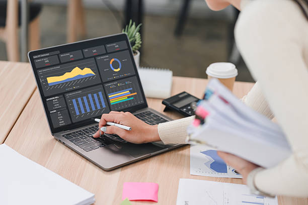 istock Businesswoman analyzing data report on laptop dashboard with charts and graphs, holding documents in modern office. 2225498766