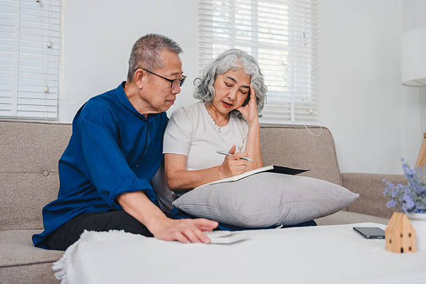istock Elderly couple discussing pension and retirement plans while sitting on sofa, with notebook and documents in cozy living room 2225498881