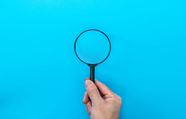 istock Man hand holding a magnifying glass on blue background 2225510036