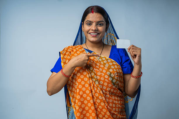 Portrait of smiling mid adult woman dressed in traditional clothing showing blank white credit cards while standing on white background