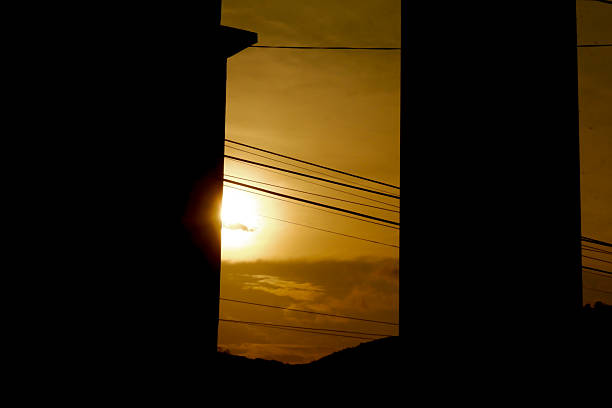 A dramatic sunset view partially obscured by buildings and intersecting power lines, capturing a moment of urban beauty with golden sky tones.