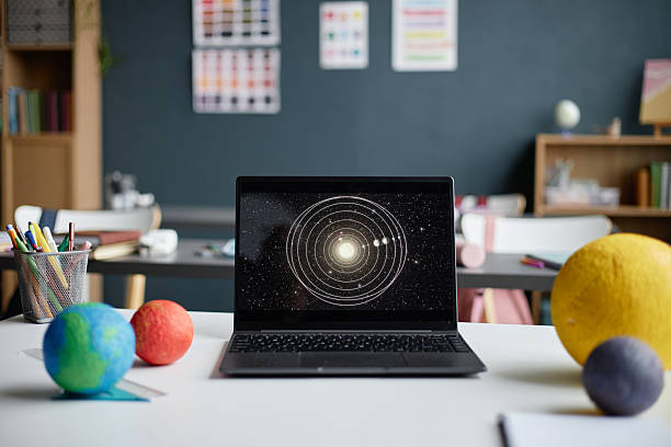 Laptop Displaying Solar System Diagram Surrounded by Planet Models in Classroom