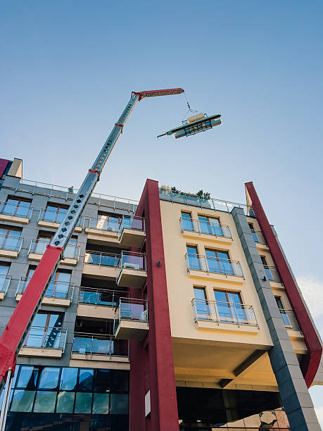 istock Crane lifting building materials during rooftop construction on modern residential building with balconies and glass railings, set against clear blue sky. Construction crane lifting building materials 2225531226