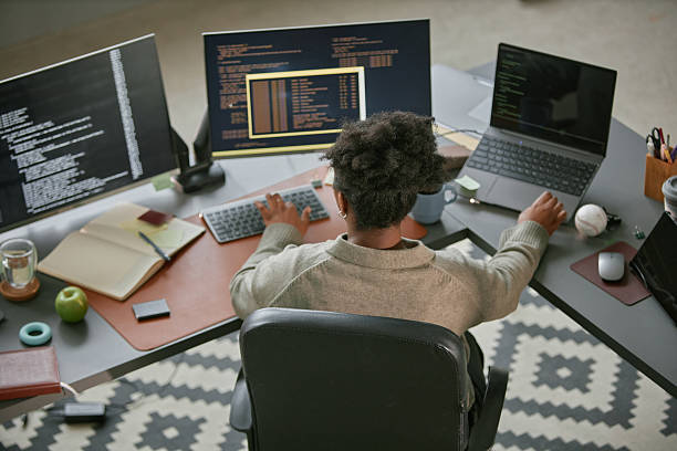 istock Young Adult Black Woman Working on Multiple Computers in Modern Office Setting 2225534930