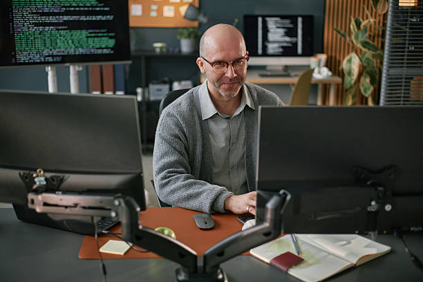 istock Portrait of Middle Aged Caucasian Man Smiling While Coding at Dual Monitors 2225534998