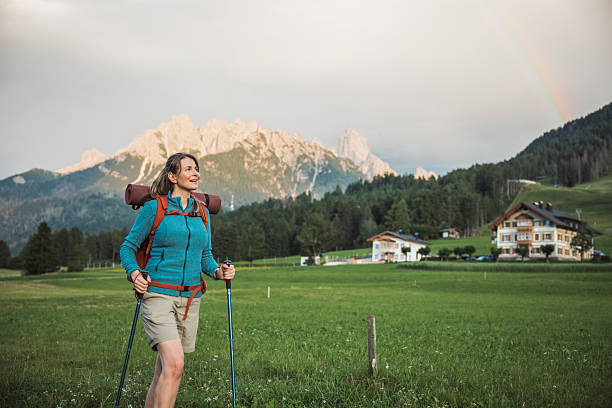 A woman hiker with a backpack walks through a lush alpine forest and valley.