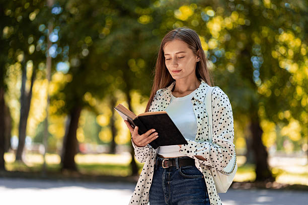 istock Young woman reading a book in a park during a sunny day 2225536514